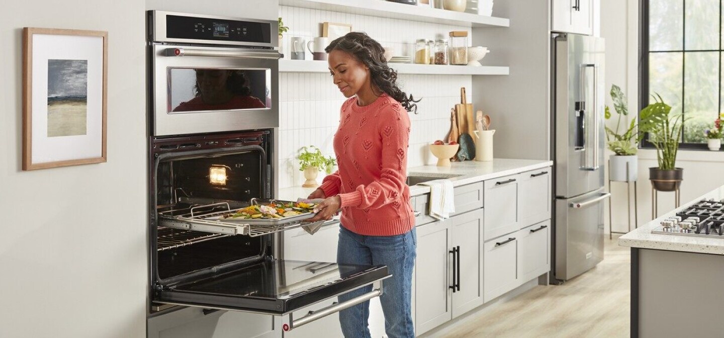 A woman pulling a dish of baked vegetables out of a combination wall oven A woman pulling a dish of baked vegetables out of a combination wall oven
